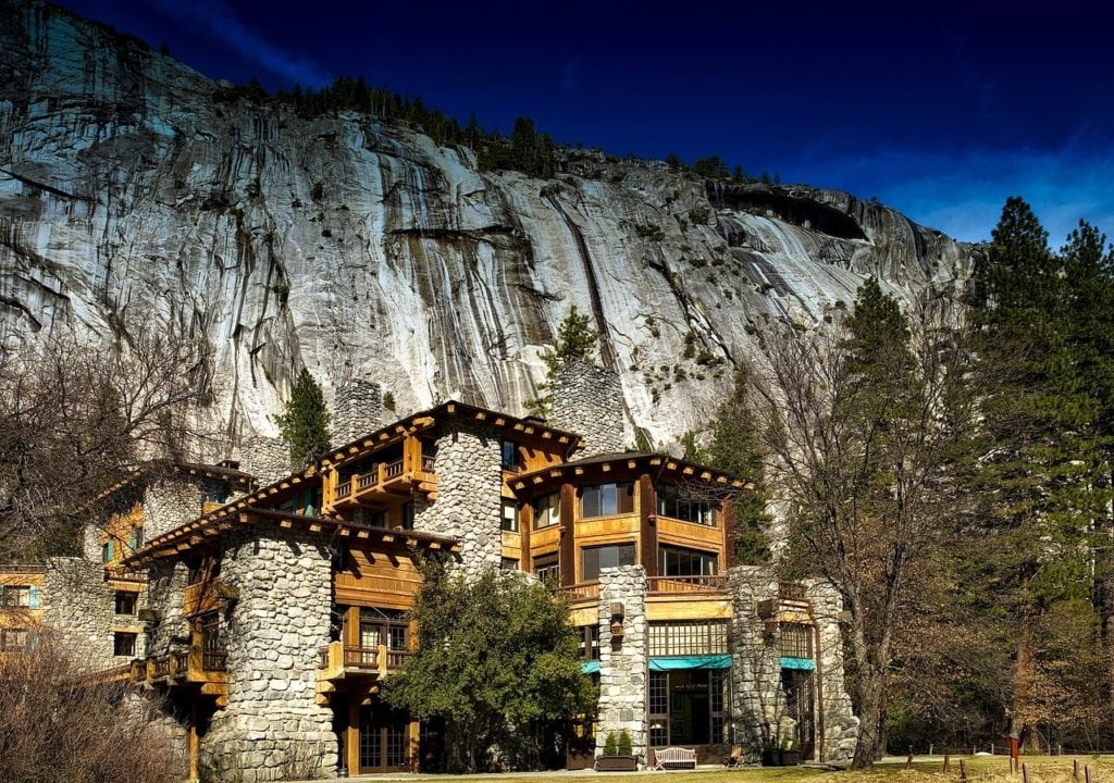 stone & log hotel in front of a large rock mountain face