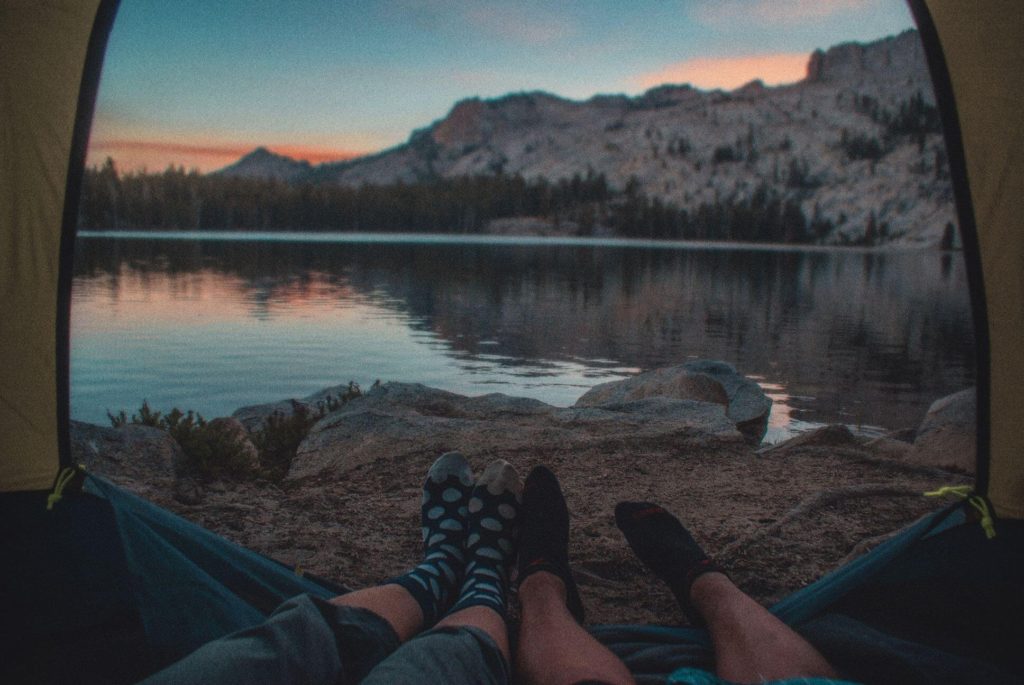 couple looking out a tent onto a lake & mountains, can see their sock-covered feet in the photo