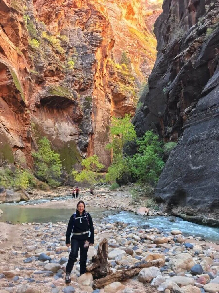 woman standing in the rocks along a shallow riverbed, surrounded by tall canyon walls