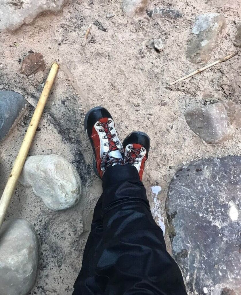 legs crossed at feet, black dry pants, water shoes, wooden hiking pole